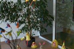 Na zdjęciu widać wielkanocne dekoracje: ozdobione gałązki z kolorowymi ptaszkami z rolek papieru, papierowe kurczaki oraz pisanki ustawione na podłodze