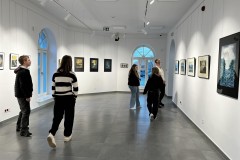 Grupa młodzieży z bursy zwiedza galerię sztuki, oglądając różnorodne prace w nowoczesnym, jasnym wnętrzu.