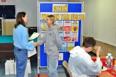 Podczas Dnia Wolontariusza wychowawczyni wręcza uczestniczce dyplom i upominek; w tle znajdują się plakaty informacyjne o wolontariacie.