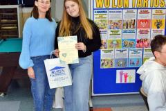 Podczas Dnia Wolontariusza wychowawczyni wręcza uczestniczce dyplom i upominek; w tle znajdują się plakaty informacyjne o wolontariacie.