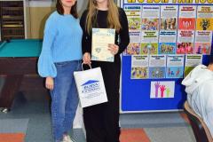 Podczas Dnia Wolontariusza wychowawczyni wręcza uczestniczce dyplom i upominek; w tle znajdują się plakaty informacyjne o wolontariacie.