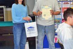 Podczas Dnia Wolontariusza wychowawczyni wręcza wolontariuszowi dyplom i upominek; w tle znajdują się plakaty informacyjne o wolontariacie.