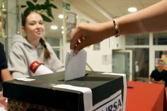 Wychowanka wrzuca karty do głosowania do urny wyborczej. W tle członek komisji wyborczej.