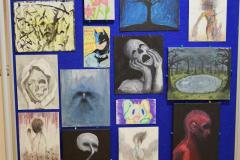 Tablica z pracami plastycznymi wychowanków bursy: kwiaty, przyroda, drzewo, twarze ludzi, martwa natura.