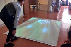 Wychowanek bursy gra  w grę z wykorzystaniem „Interaktywnej Podłogi  – Pakiet Rozwój Mózgu” w Bibliotece Pedagogicznej.