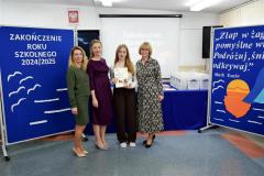 Wychowanka  z  dwójką wychowawców i Panią Dyrektor na tle tablic z dekoracjami zakończenia roku szkolnego.