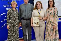 Wychowanka z dwójką wychowawców  i Panią Dyrektor pozują do zdjęcia na tle tablic z dekoracjami zakończenia roku szkolnego.