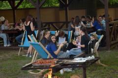 Wychowankowie zgromadzeni w altanie i wokół  ogniska na krzesłach turystycznych