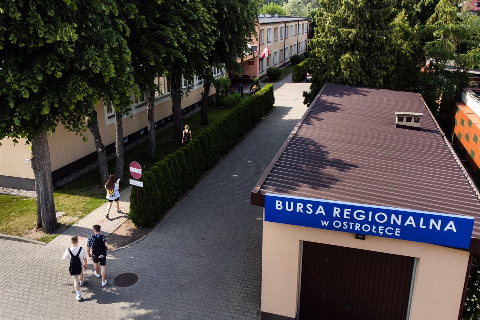 Widok z lotu ptaka na plac Bursy od strony wjazdu widoczny garaż i wychowankowie podążający do wejścia głównego budynku Bursy.