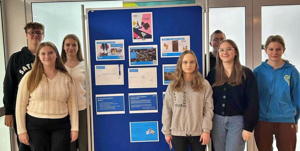 Grupa wychowanków pozuje do zdjęcia na tle wystawy przygotowanej z okazji Tygodnia Edukacji Globalnej