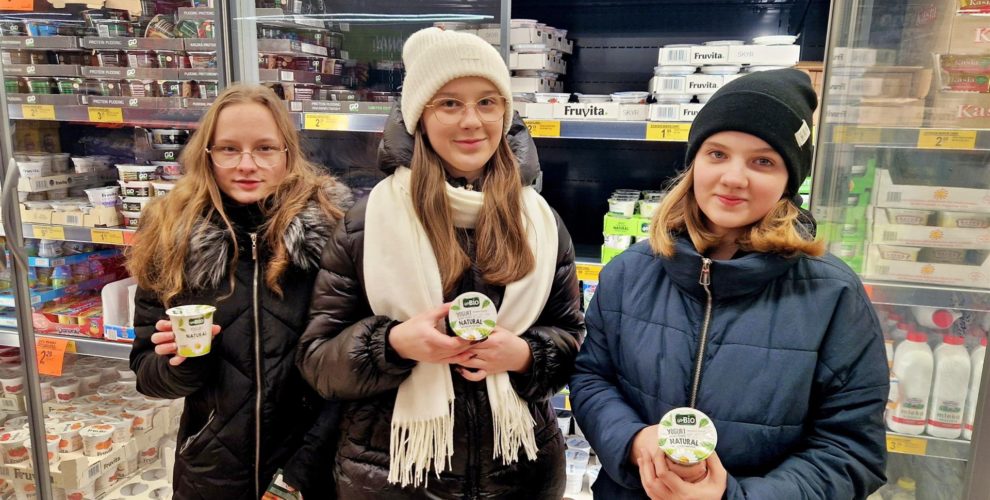 Wychowanki trzymające bio jogurty w sklepie spożywczm na tle chłodni wypełnionych artykułami spożywczymi