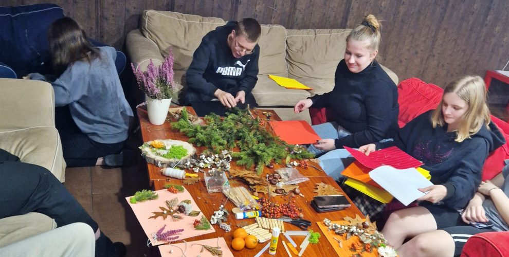 Wychowankowie zgromadzeni wokół stolików, na których leżą materiały: szyszki, liście, farby
