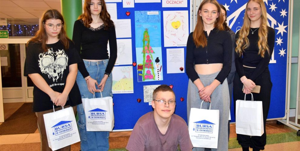 Uczestnicy konkursu "Miłość w moich oczach" pozują na tle wystawy swoich prac w holu Bursy