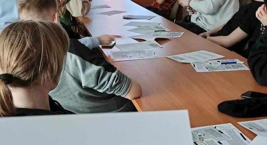 Wychowankowie oglądają film. Na stole leżą materiały potrzebne do zajęć.
