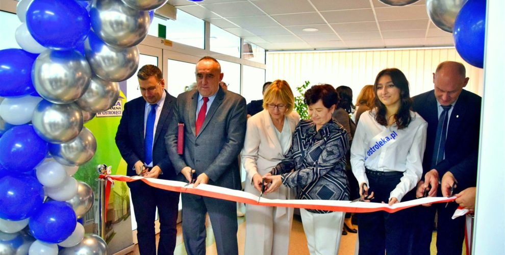 Moment symbolicznego przecięcia wstęgi podczas uroczystego otwarcia stołówki oraz kuchni w Bursie Regionalnej w Ostrołęce. Przedstawiciele młodzieży oraz goście uśmiechają się trzymając w ręku skrawki wstęgi.