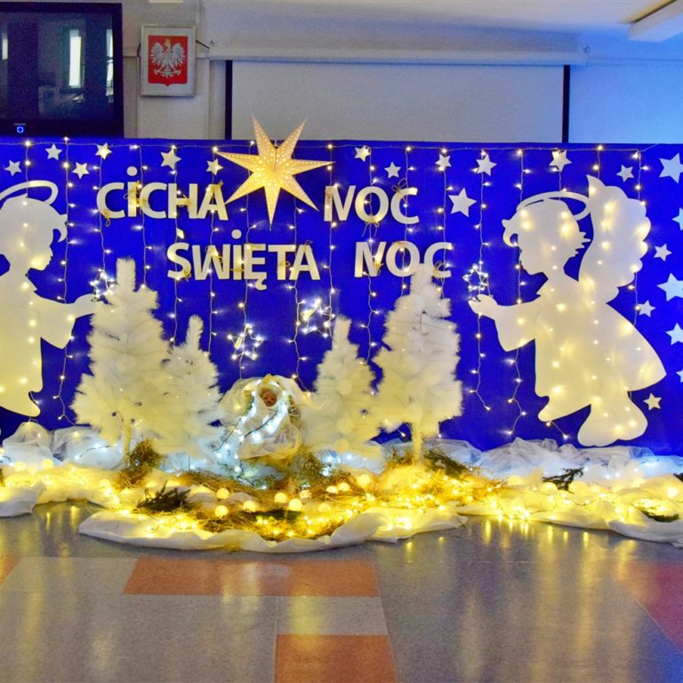 Niebieska tablica na której znajdują się: wycięte z papieru białe gwiazdki, 2 białe anioły, lampki, 4 białe choinki. Pośrodku w drewnianym żłóbku leży postać Jezusa. Na tablicy znajduje się napis: Cicha noc, święta noc. Nad nim wisi biała duża gwiazda. Na podłodze znajduje się biała tkanina, na której leżą zapalone lampki. Z boku stoi zielona choinka udekorowana bombkami.