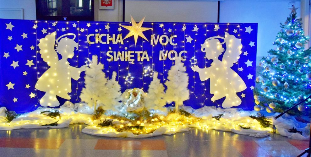 Niebieska tablica na której znajdują się: wycięte z papieru białe gwiazdki, 2 białe anioły, lampki, 4 białe choinki. Pośrodku w drewnianym żłóbku leży postać Jezusa. Na tablicy znajduje się napis: Cicha noc, święta noc. Nad nim wisi biała duża gwiazda. Na podłodze znajduje się biała tkanina, na której leżą zapalone lampki. Z boku stoi zielona choinka udekorowana bombkami.