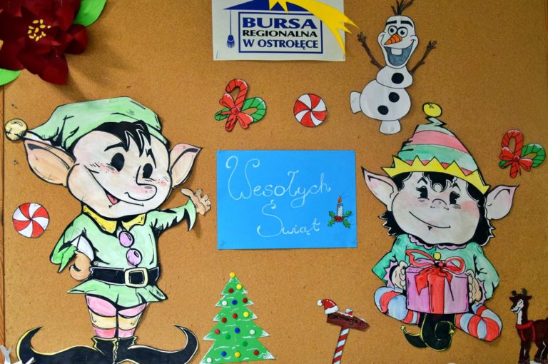 Zdjęcie przedstawia świąteczną gazetkę, na której znajdują się dwa kolorowe elfy wykonane z papieru. Pośrodku umieszczono biały napis „Wesołych Świąt” na niebieskim tle. Całość uzupełniają barwne dekoracje świąteczne wykonane przez młodzież, a w górnej części gazetki widnieje kolorowy logotyp Bursy