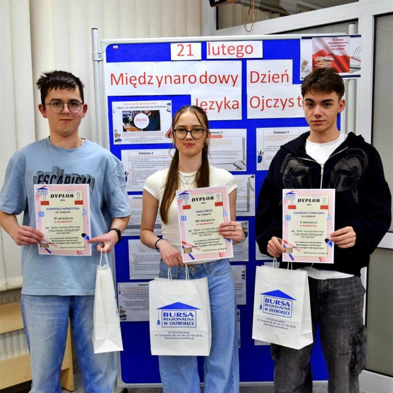 Troje wychowanków stoi przy tablicy na której znajduje się napis: 21 lutego Międzynarodowy Dzień Języka Ojczystego. W rękach trzymają dyplomy i nagrody rzeczowe.