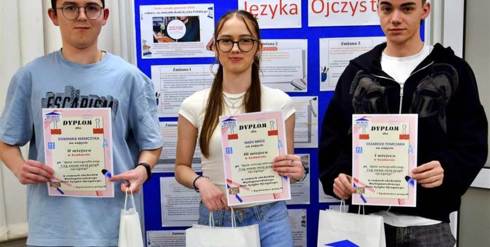 Troje wychowanków stoi przy tablicy na której znajduje się napis: 21 lutego Międzynarodowy Dzień Języka Ojczystego. W rękach trzymają dyplomy i nagrody rzeczowe.