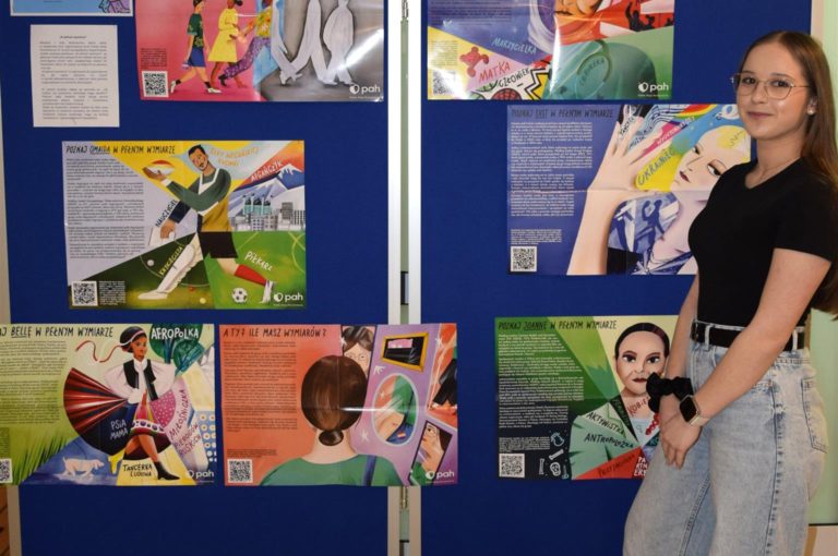 Wychowanka pozuje do zdjęcia na tle wystawy „W pełnym wymiarze”.