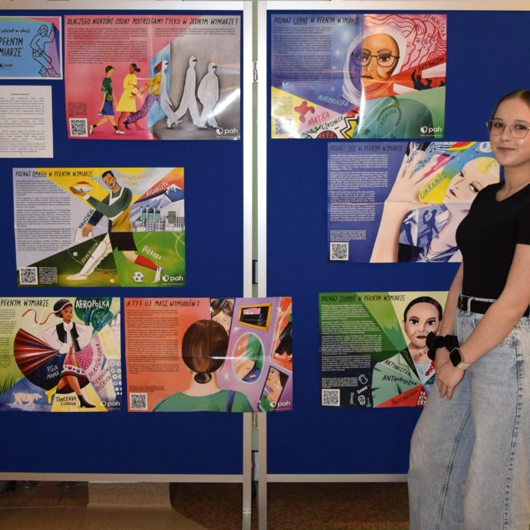 Wychowanka pozuje do zdjęcia na tle wystawy „W pełnym wymiarze”.