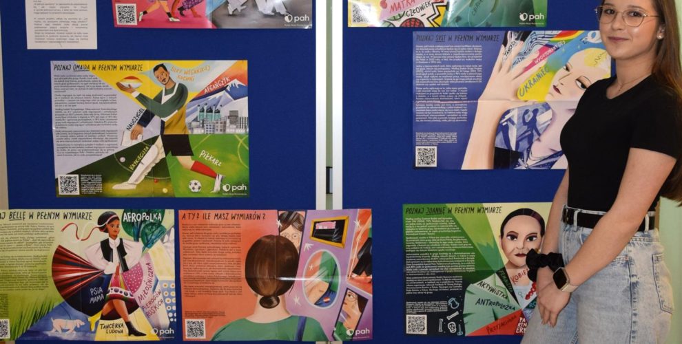 Wychowanka pozuje do zdjęcia na tle wystawy „W pełnym wymiarze”.