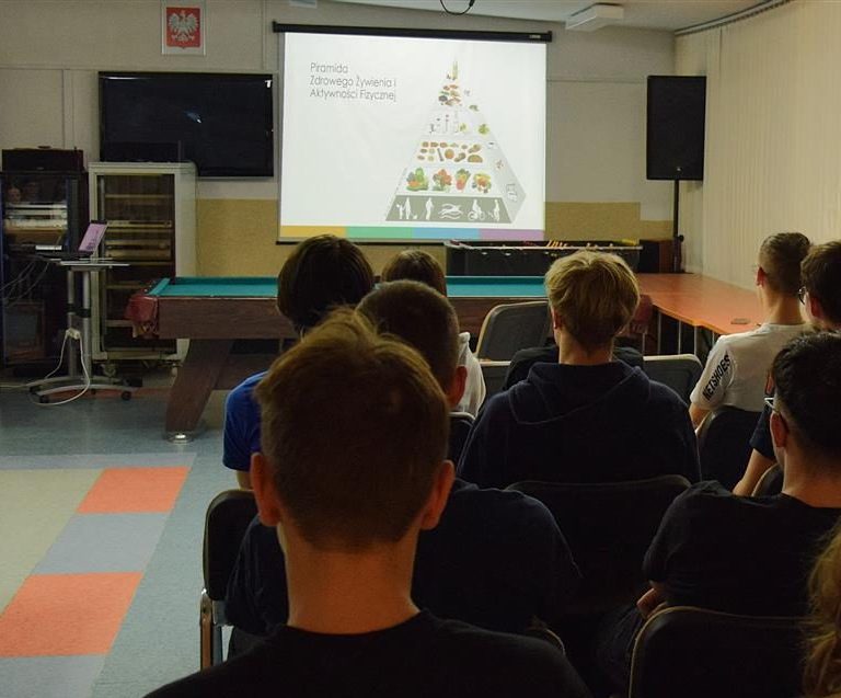 Młodzież siedząca na krzesłach oraz Pani dietetyk przedstawiająca informacje