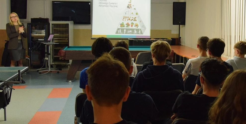 Młodzież siedząca na krzesłach oraz Pani dietetyk przedstawiająca informacje