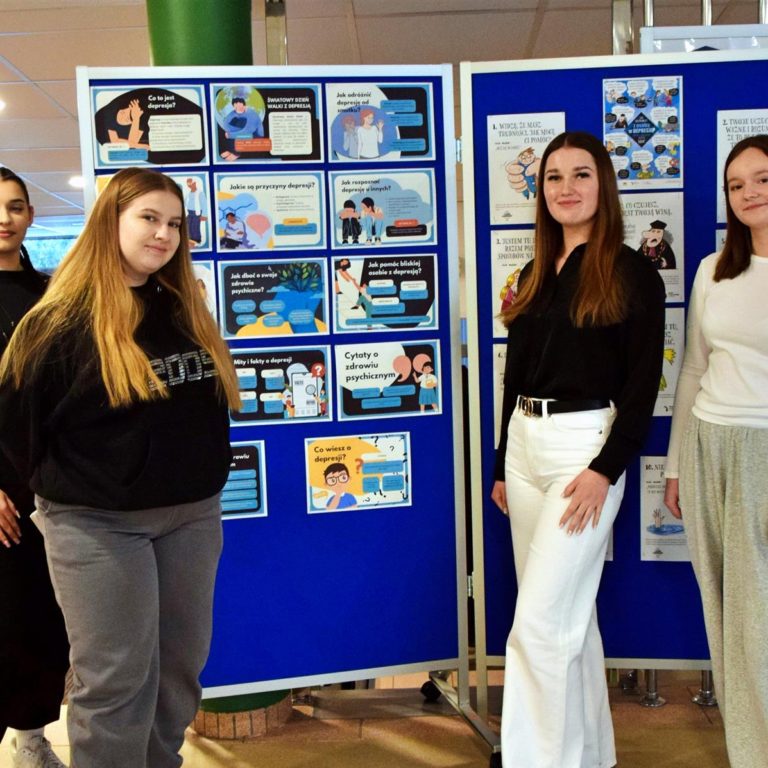 Grupa wychowanków stoi przy wystawie przygotowanej z okazji „Światowego Dnia Walki z Depresją”.
