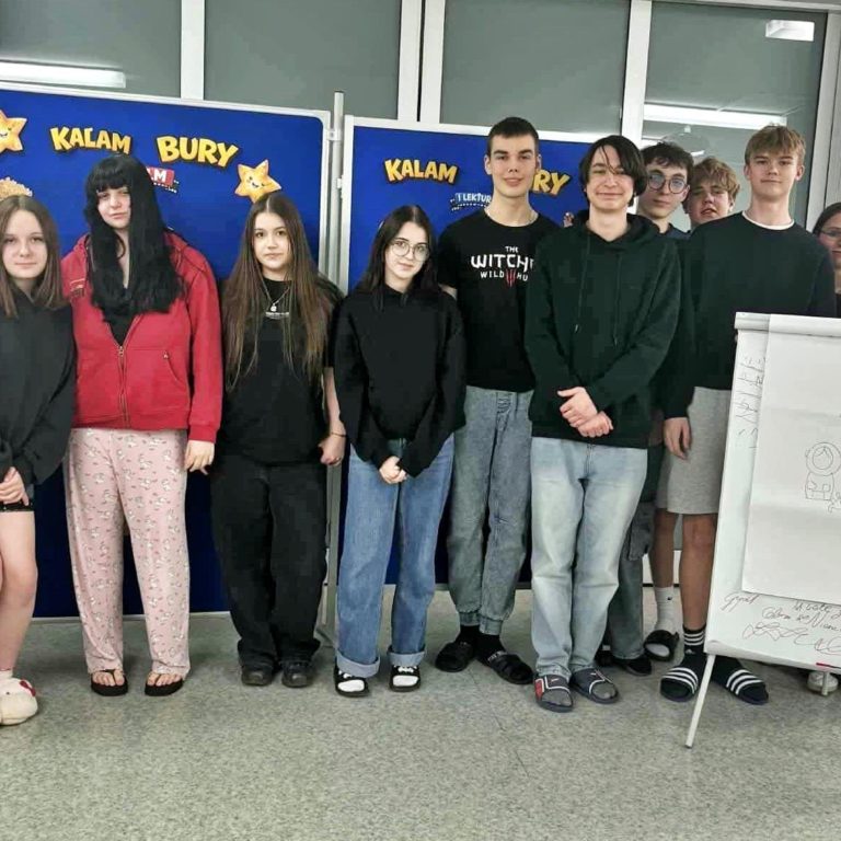 Wychowankowie bursy stoją razem przy dekoracji związanej z kalamburami. Wspólne zdjęcie pokazuje dobrą zabawę i integrację młodzieży