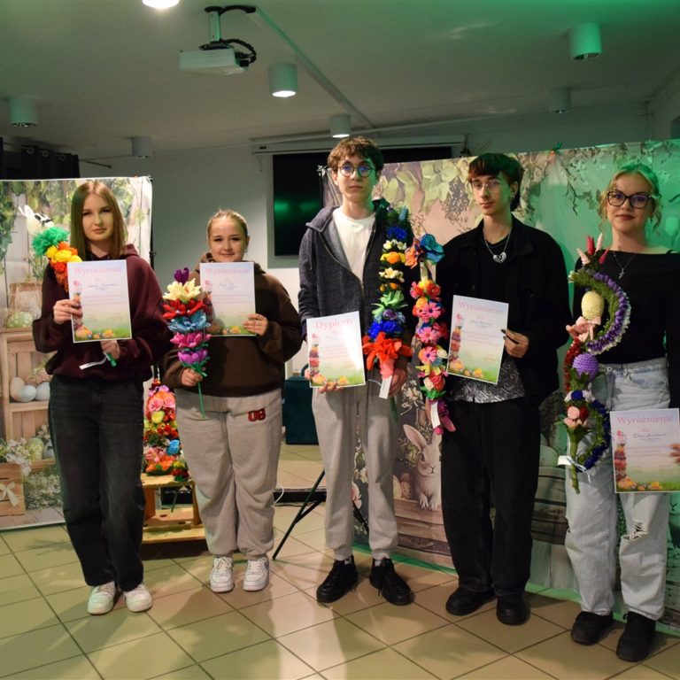 Pięcioro wychowanków Bursy Regionalnej w Ostrołęce stoi w rzędzie . W rękach trzymają różnokolorowe palmy wielkanocne (kurpiowskie) oraz dyplomy za udział w III międzyinternackim konkursie plastycznym na „Palmę Wielkanocną”. Za nimi znajduje się po obu stronach płótno z namalowanymi ozdobami wiosenno-wielkanocnymi: kolorowe pisanki, kwiaty, zajączki, bazie).