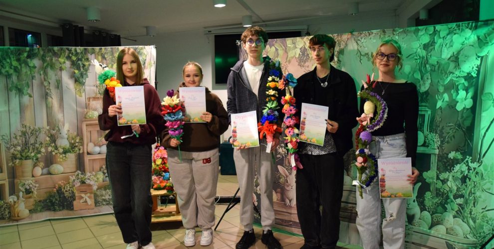 Pięcioro wychowanków Bursy Regionalnej w Ostrołęce stoi w rzędzie . W rękach trzymają różnokolorowe palmy wielkanocne (kurpiowskie) oraz dyplomy za udział w III międzyinternackim konkursie plastycznym na „Palmę Wielkanocną”. Za nimi znajduje się po obu stronach płótno z namalowanymi ozdobami wiosenno-wielkanocnymi: kolorowe pisanki, kwiaty, zajączki, bazie).