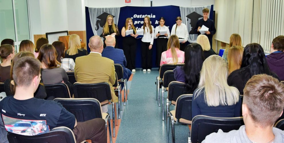 Grupa młodzieży stoi na scenie podczas uroczystego pożegnania maturzystów, a przed nimi siedzi publiczność.