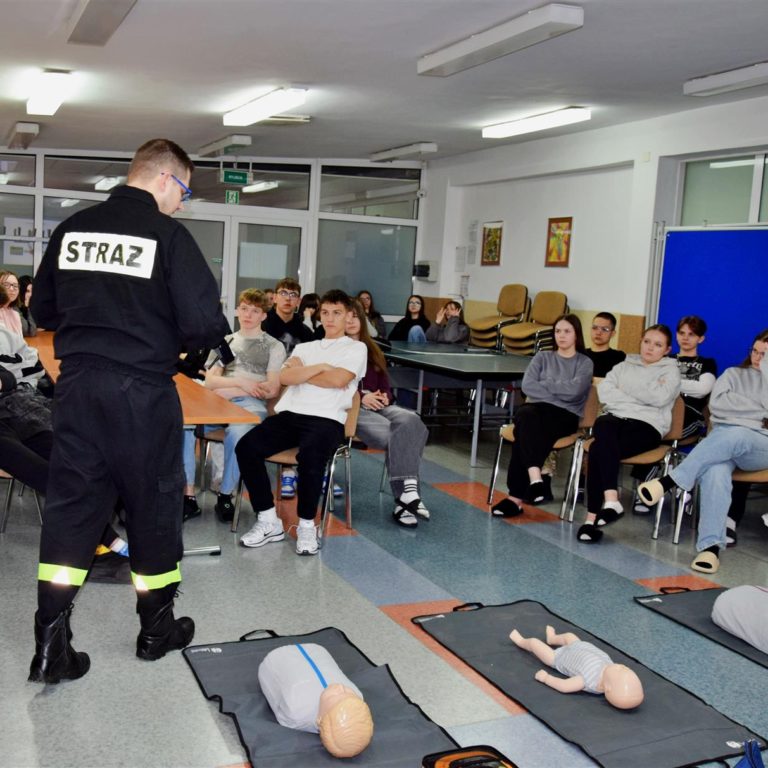 Wychowankowie siedzący na krzesłach oraz słuchający Strażaka, na podłodze leżące fantomy