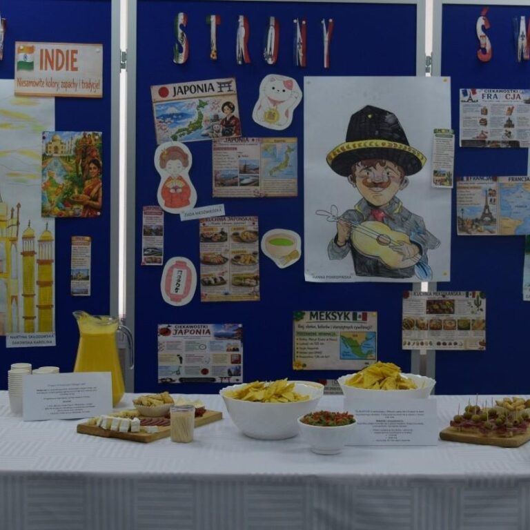 Na zdjęciu widać kolorową wystawę poświęconą kulturze różnych krajów świata, takich jak Indie, Japonia, Meksyk i Francja, ozdobioną plakatami, rysunkami oraz tradycyjnymi przekąskami.
