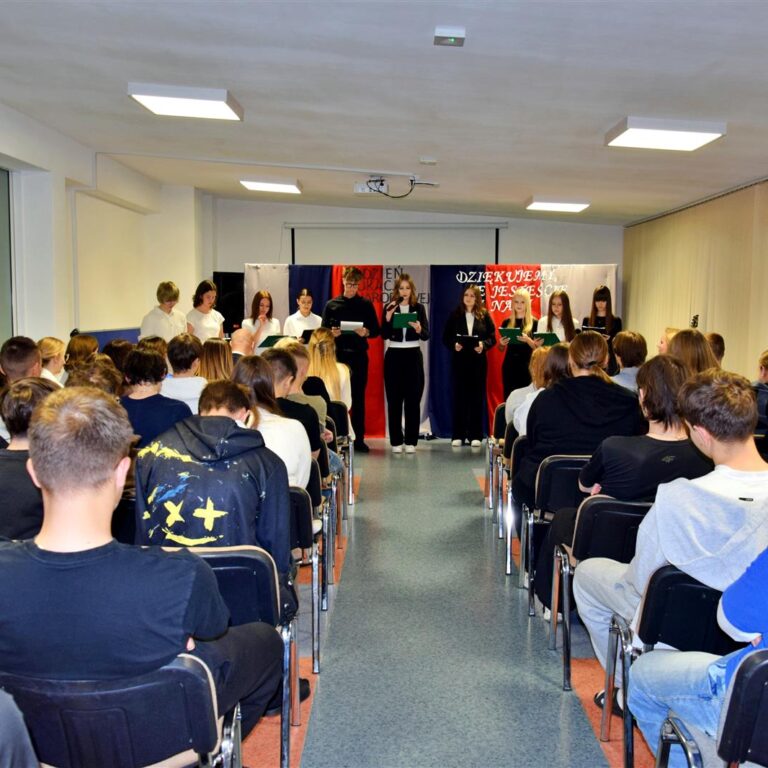 Młodzież i wychowawcy podczas części artystycznej z okazji Dnia Edukacji Narodowej. W tle dekoracja, na pierwszym planie występujący wychowankowie, a przed nimi zgromadzona publiczność.