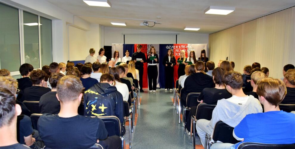 Młodzież i wychowawcy podczas części artystycznej z okazji Dnia Edukacji Narodowej. W tle dekoracja, na pierwszym planie występujący wychowankowie, a przed nimi zgromadzona publiczność.